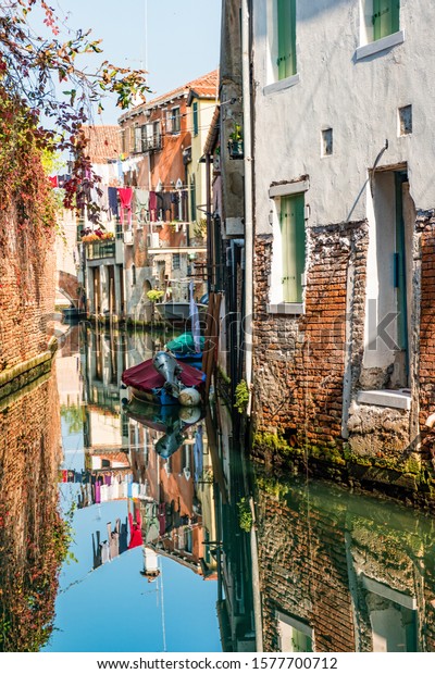 Traditional canal street\
with reflection in the water laundry hanging out of a typical\
Venetian facade.\
Italy.