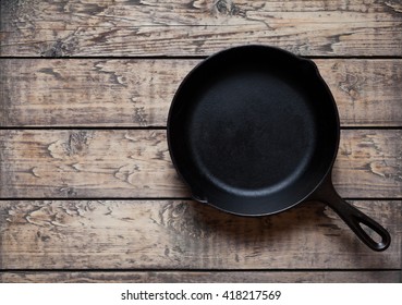 Traditional cast iron skillet pan on vintage wooden table background. Kitchen equipment