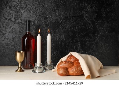 Traditional challah bread with wine and glowing candles on dark background. Shabbat Shalom