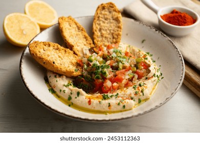 Traditional chickpea hummus with cut pepper and onion in the center served with toast.