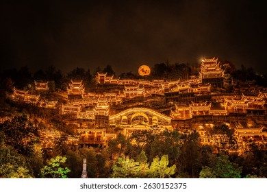 Arquitectura tradicional china que brilla intensamente por la noche en la ciudad del valle de Wangxian con una luna llena que se eleva detrás de la montaña, creando una atmósfera mágica y serena.