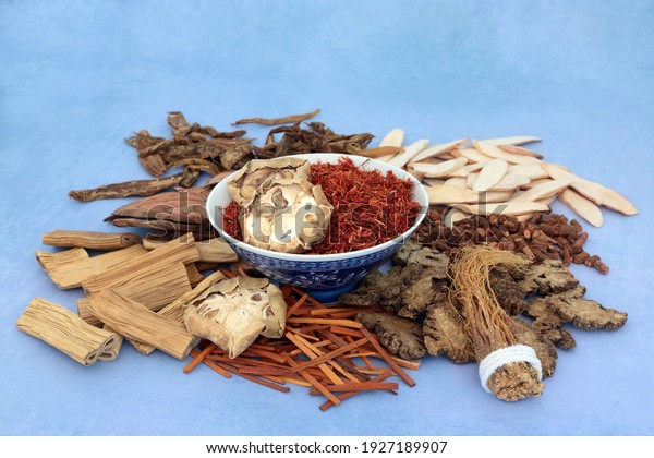 Traditional Chinese herbs and spice used in\
traditional herbal medicine in a bowl and loose on mottled blue\
background. Natural healthcare\
concept.