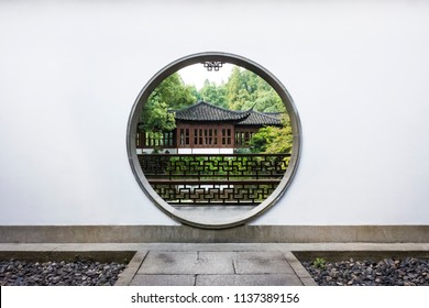 Traditional Chinese house among trees viewed through a circular moon gate and white wall in Guo's Villa (Guo Zhuang), a traditional Chinese Garden near West Lake, Hangzhou, China