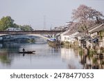 Traditional Chinese housing with a large pink flower tree and bridge along river in the spring of Wuzhen, Zhejiang, China. A fisherman and his boat are in the river. 