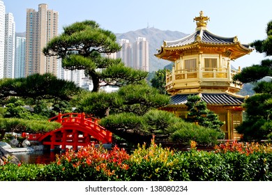 Traditional Chinese style golden pagoda in the garden decorated with red bridge across the pond. Cityscape with lots of skyscrapers in the background