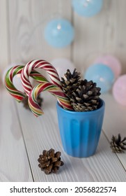 traditional christmas decoration, colorful candycanes and cones in the blue cup on white wooden background