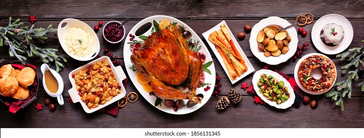 Traditional Christmas Turkey Dinner. Top View Panoramic Table Scene On A Dark Wood Banner Background. Turkey, Potatoes And Sides, Stuffing, Fruit Cake And Plum Pudding.