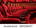 Traditional classically regal ornate rounded wood armed formal plush deep red velvet opera movie theater chairs in curved row with decorative gold molding in fancy carpeted venue
