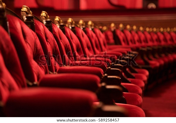 Traditional\
classically regal ornate rounded wood armed formal plush deep red\
velvet opera movie theater chairs in curved row with decorative\
gold molding in fancy carpeted\
venue