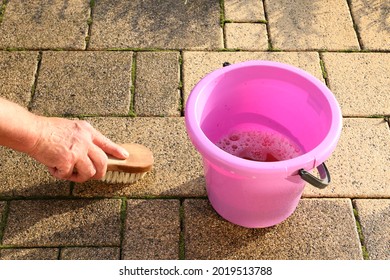 Traditional Cleaning Of Dirty Paving Stones In The Garden With Water And A Brush.