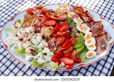 Traditional Cobb salad in a large oval plate on a checkered tablecloth. Summer sunny day. - Powered by Shutterstock