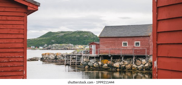 Traditional cod fishing sheds in Salvage, Newfoundland and Labrador, Canada. Red wooden buildings and piers. Rocks and reflections. Mountain in the background. Rural, Rugged, beautiful Newfoundland. - Shutterstock ID 1999211444