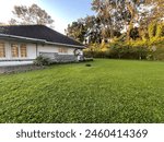 Traditional colonial 1 story house in east java indonesia with a huge plot of grass and trees surrounding it.