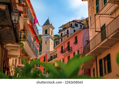 Traditional colorful houses on a street in old town with a view of the bell tower of Chiesa di San Lorenzo, Manarola in Cinque Terre, Italy