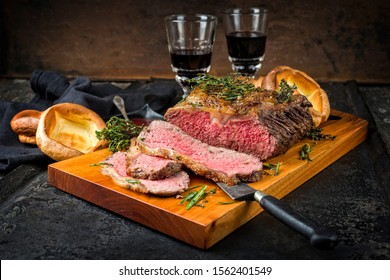 Traditional Commonwealth Sunday roast with sliced cold cuts roast beef with herbs and Yorkshire pudding closeup on a modern design wooden board 
