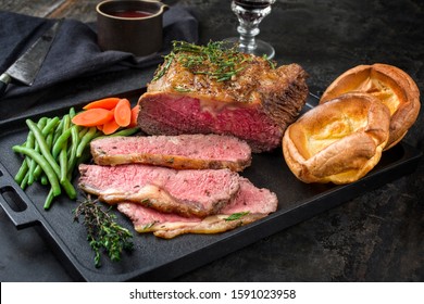 Traditional Commonwealth Sunday roast with sliced cold cuts roast beef with vegetable and Yorkshire pudding as closeup on a modern design cast iron tray 