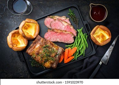 Traditional Commonwealth Sunday roast with sliced cold cuts roast beef with vegetable and Yorkshire pudding as top view on a modern design cast iron tray 