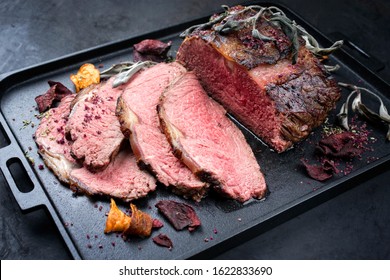 Traditional Commonwealth Sunday roast with sliced cold cuts roast beef with vegetable chips and herbs as closeup on a modern design tray 
