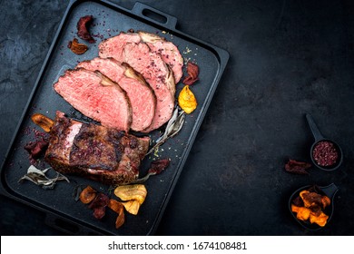 Traditional Commonwealth Sunday roast with sliced cold cuts roast beef with vegetable chips and herbs as top view on a modern design tray with copy space right 
