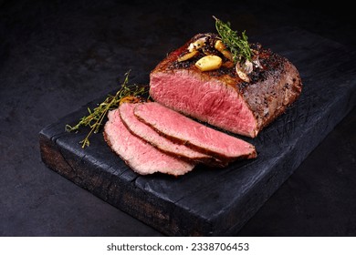 Traditional Commonwealth Sunday roast with sliced cold cuts roast beef with garlic and salt as close-up on a rustic charred wooden board  - Shutterstock ID 2338706453