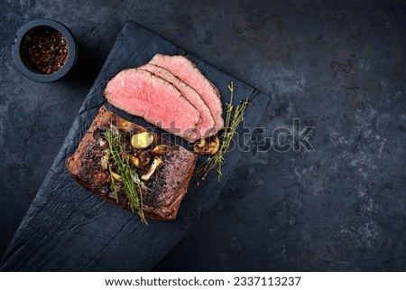 Traditional Commonwealth Sunday roast with sliced cold cuts roast beef with garlic and salt as top view on a rustic charred wooden board with copy space