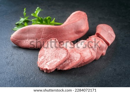 Traditional cooked beef tongue with herbs offered as close-up on a rustic black board 