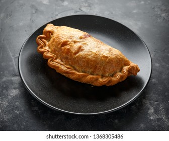 Traditional Cornish pasty filled with beef meat, potato and vegetables on black plate - Shutterstock ID 1368305486