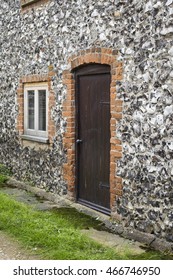 Traditional countryside cottage door and window set against a rough cut flint wall.