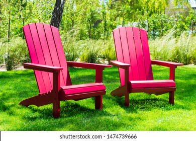 Traditional curveback sunset red plastic outdoor patio adirondack chairs with contoured backs and seats on green grass of outdoor lawn. Design, concept, idea.