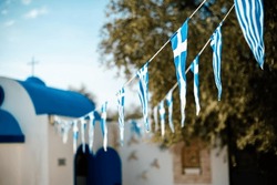 Traditional Cypriot Church With Blue Roof And White Wall. Symbolic Flags Hanging Near With Growing Olive Trees Around.