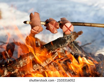 Traditional Czech barbecue - sausages on a stick roasted on the campfire. Sausages on the stick grilled in the fire. Winter forest. Concept of outdoor adventure and seasonal winter vacation.