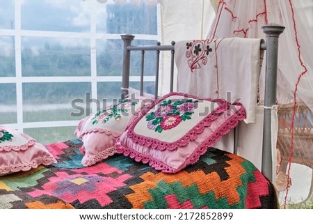 Traditional decoration of iron bed in Tatar vintage style. Woven colorful bedspread, small pillows decorated with embroidery ribbons with floral pattern and braid, crocheted. Folk festival Sabantuy.