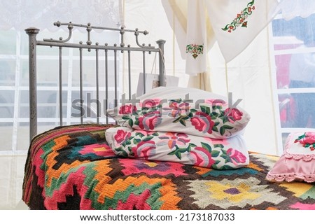 Traditional decoration of iron bed in Tatar vintage style. Woven colorful bedspread, pillows decorated with floral embroidery with smooth surface. Folk festival Sabantuy.