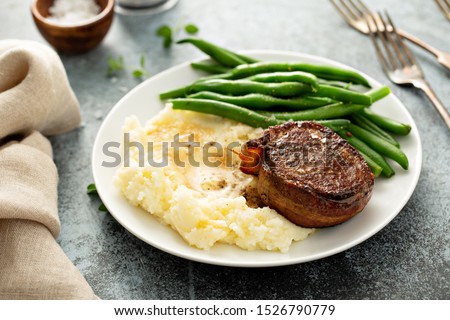Traditional dinner meal with a bacon wrapped steak, green beans and mashed potatoes