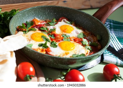 Traditional Dish Of Israeli Cuisine Shakshuka. Fried Eggs With Tomatoes, Peppers, Onions, Cilantro And Pita In A Pan On Light Green Background