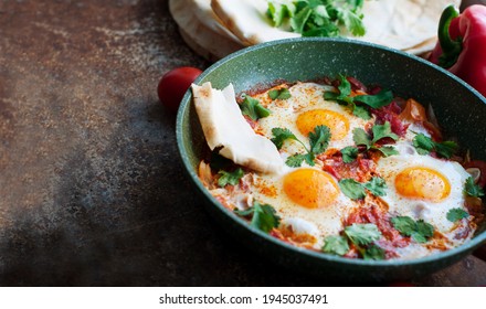 Traditional Dish Of Israeli Cuisine Shakshuka. Fried Eggs With Tomatoes, Peppers, Onions, Cilantro And Pita In A Pan On Dark Brown Background