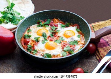 Traditional Dish Of Israeli Cuisine Shakshuka. Fried Eggs With Tomatoes, Peppers, Onions, Cilantro And Pita In A Pan On Dark Brown Background