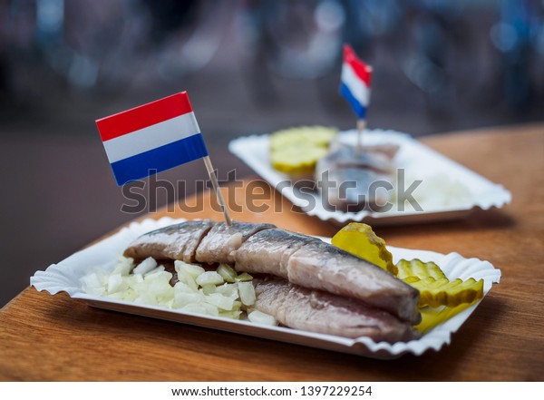 Traditional Dutch street food - saline herring\
with pickles, onions and Dutch flags in a fish. Still life with the\
Amsterdam snack in a soft\
focus.