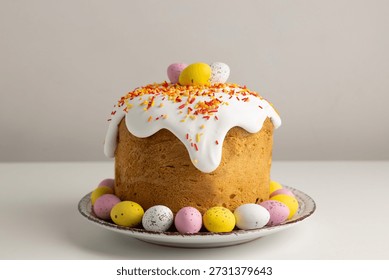 Traditional Easter cake with white icing, colorful sprinkles, and chocolate eggs on the top, served on a plate together with colorful eggs.