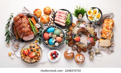 Traditional Easter dinner or  brunch with ham, colored eggs, hot cross buns, cake and vegetables. Easter meal dishes with holday decorations. Top view, flat lay - Shutterstock ID 2248374733