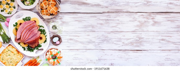 Traditional Easter Ham Dinner. Top Down View Side Border On A White Wood Banner Background With Copy Space. Ham, Scalloped Potatoes, Eggs, Hot Cross Buns, Carrot Cake And Vegetables.