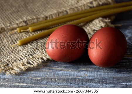 Traditional easter red dyed eggs with beeswax candles on rustic wooden and burlap background