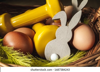 Traditional Easter wicker basket with eggs, decorative bunny and yellow dumbbells. Easter fitness and training composition.