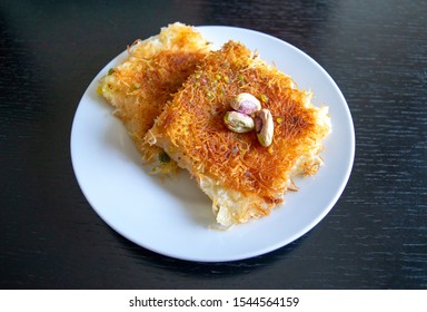 Traditional eastern dessert kunafa. Top view. Arabic cheese kunafa in white plate on dark wooden  table. Konafa. 