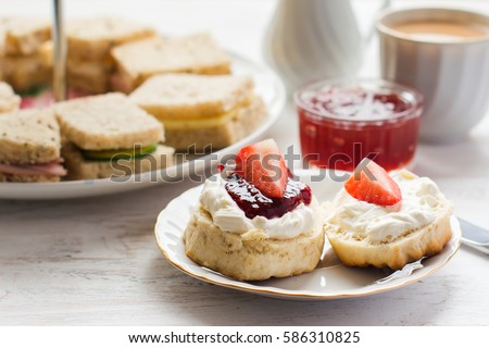 Traditional English afternoon tea: scones with clotted cream and jam, strawberries, with various sandwiches on the background, selective focus