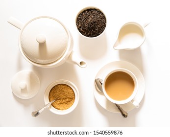 Traditional English Breakfast Black Tea With Milk -tea Leaves. Teacup, Teapot, Sugar And Milk Bowls On A White Background, Top View. Daylight. Close-up.