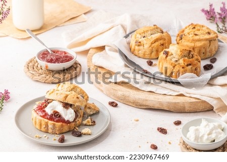 Traditional English pastries for afternoon tea: scones. Homemade raisin scones with clotted cream and homemade strawberry jam. Scones on plate served with milk on table