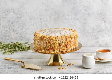 Traditional Esterhazy Cake With Almond On Golden Cake Stand Over White Background With Cup Of Coffee And Cake Spatula. Side View, Copy Space