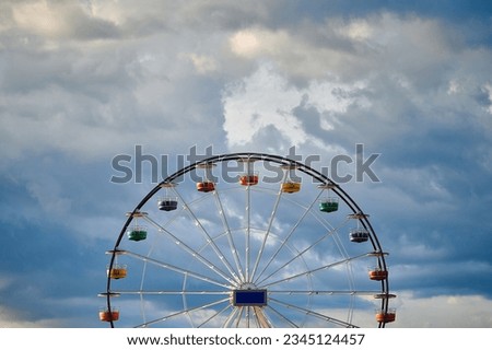 Traditional ferris wheel with colorful carriages at sunrise in a tourist town. Dramatic clouds in the background.