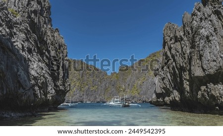 Traditional Filipino double-outrigger dugout  bangka  boats are anchored in a lagoon surrounded by picturesque karst rocks. Green vegetation on steep slopes. Clear blue sky. Philippines. Secret lagoon